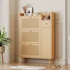 A wooden shoe cabinet with rattan doors and a drawer, placed in a room with a plant and a rug. Podgląd zdjęcia produktu