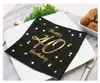 A black napkin with gold polka dots and 'Happy 40 Birthday' text is placed on a white plate, set on a table with cutlery and a small plant. Náhled obrázku produktu