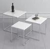 Three nesting tables with white tops and silver metal frames are arranged on a light gray floor against a white wall. Produktbild-Vorschau