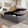 A bed with storage is shown in a bedroom setting with a wall art and a window in the background. Podgląd zdjęcia produktu