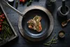 A cooked steak in a pan with rosemary, surrounded by ingredients like tomatoes, peppers, and spices. Produktbild-Vorschau