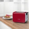 A red Bosch toaster sits on a wooden countertop next to two slices of toast with jam. Produktbild-Vorschau