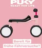 A pink balance bike with black seat and wheels against a pink background. Voir les images du produit