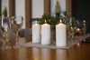 Three white pillar candles are lit on a table, set with wine glasses and greenery. Anteprima dell’immagine prodotto