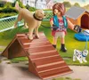 A Playmobil girl is training two dogs in a park-like setting with a dog house and agility equipment. Produktbild-Vorschau