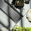 A close-up view of a brushed steel shower drain with rocks and plants in the background. Anteprima dell’immagine prodotto