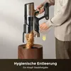 A person is emptying a cordless vacuum cleaner into a wooden bin. Produktbild-Vorschau
