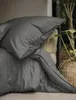 A close-up view of a grey striped duvet and pillowcase set, with a woven basket and plant in the background. Produktbild-Vorschau