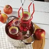 A jar lifter is used to place a jar of red jam into a pot of water, with apples in the background. Anteprima dell’immagine prodotto