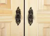 A close-up view of two ornate dark brown handles on light-colored wooden doors. Produktbild-Vorschau