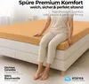A woman sitting on a bed with an orange fitted sheet. Produktbild-Vorschau