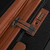 A close-up view of a black suitcase with brown leather accents, showing the zipper, zipper pulls, and a TSA combination lock. Podgląd zdjęcia produktu