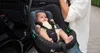 A person is holding a baby in a car seat next to an open car door. Podgląd zdjęcia produktu