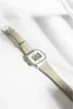 A digital watch with a gray band is placed on a white surface with soft shadows. Produktbild-Vorschau