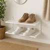 Two pairs of shoes displayed on a white wall-mounted shoe rack. A plant in a wicker basket is on the left. Produktbild-Vorschau