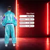 A person wearing a tracksuit stands in front of a brick wall with neon lights, next to a size chart. Produktbild-Vorschau