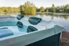 A close-up view of a hot tub filled with water, set against a backdrop of a calm lake and trees. Produktbild-Vorschau