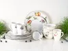 A collection of porcelain dinnerware with fruit motifs, including plates, bowls, and mugs, arranged on a white surface with some greenery and blueberries. Náhľad obrázku produktu