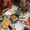 People enjoying a meal outdoors at a table set with food and plates. Podgląd zdjęcia produktu