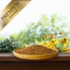 A wooden bowl filled with birdseed sits on a wooden surface, with a blurred background of green foliage and yellow flowers. A golden ribbon with the word "PREMIUM" and stars is overlaid in the top left corner. Produktbild-Vorschau