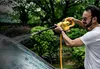 A man is using a yellow pressure washer to clean a car in an outdoor setting with lush greenery. Podgląd zdjęcia produktu