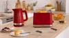 A red Bosch toaster and kettle are displayed on a kitchen counter with breakfast items. Voir les images du produit