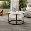 A round coffee table with a marble-like top and black metal legs is placed on a gray rug in a living room. Two vases and a glass of water are on the table. A sofa and a window with a view of trees are visible in the background. Anteprima dell’immagine prodotto