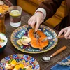 A person is cutting a piece of salmon on a decorative plate, with other dishes and a glass of water visible. Náhled obrázku produktu
