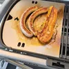 Sausages and a piece of bacon are being grilled on a metal griddle on a portable grill. Produktbild-Vorschau