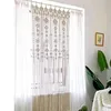 A macrame curtain hanging in a window with sheer white curtains behind it. Produktbild-Vorschau