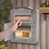 A hand is placing an envelope into a rustic vintage metal mailbox mounted on a wooden wall. Podgląd zdjęcia produktu