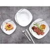 A table setting with three square plates, one with pancakes and berries, one with sliced steak and rosemary, and one empty bowl. Cutlery is also present. Náhľad obrázku produktu