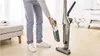 A person is using a cordless vacuum cleaner in a living room. Produktbild-Vorschau