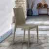 A single beige poly rattan chair is placed on a stone patio in front of a stone wall and stairs. Produktbild-Vorschau
