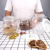 A person is holding a glass jar filled with dried flowers, with other jars and dried fruit slices on a checkered surface. Produktbild-Vorschau