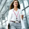 A woman walking outdoors with a coffee and a lanyard with an ID card. Produktbild-Vorschau