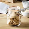 A glass jar filled with cookies sits on a wooden table next to an open book and a bowl of cereal. Anteprima dell’immagine prodotto