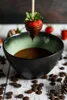 A chocolate-dipped strawberry is being held over a bowl of chocolate. Produktbild-Vorschau