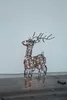 A wireframe reindeer decoration with LED lights stands on a wooden surface in front of a textured wall. Podgląd zdjęcia produktu