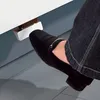 A person's foot in a black shoe is pressing down on a silver and chrome foot pedal attached to a white surface. Produktbild-Vorschau