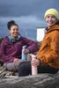 Two women sitting on a log on a beach, holding water bottles. Produktbild-Vorschau