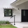 A black metal handrail is installed on the steps of a white house, next to a window with a striped awning. Podgląd zdjęcia produktu