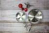 Two stainless steel frying pans and kitchen accessories are laid out on a wooden surface. Podgląd zdjęcia produktu