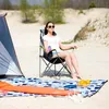 A woman is sitting in a camping chair next to a tent on a sandy beach. Produktbild-Vorschau