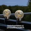 Two solar-powered globe lights with fairy lights inside are placed on a dark railing outdoors. Produktbild-Vorschau