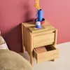A wooden nightstand with two drawers, one of which is open, next to a bed. Decorative items are on top of the nightstand. Produktbild-Vorschau