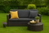 An outdoor sofa with cushions and a coffee table on a grassy lawn, surrounded by greenery. Voir les images du produit