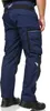 A person wearing navy blue work pants with black accents and shoes, shown from the side. Produktbild-Vorschau