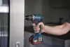 A person is using a blue and black Bosch cordless drill to screw into a white door frame. Voir les images du produit