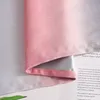 A close-up of a fabric with a pink and gray gradient, placed over an open book. Produktbild-Vorschau